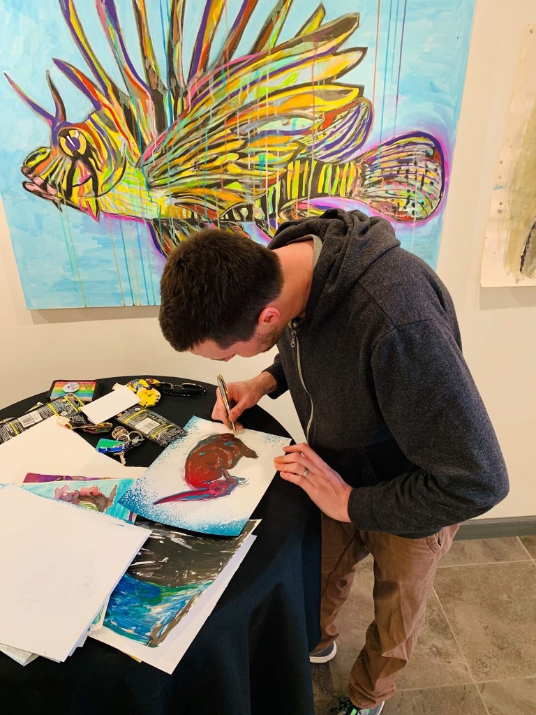 Visual artist Russell Frantom seen in an art gallery signing custom lithograph artwork 