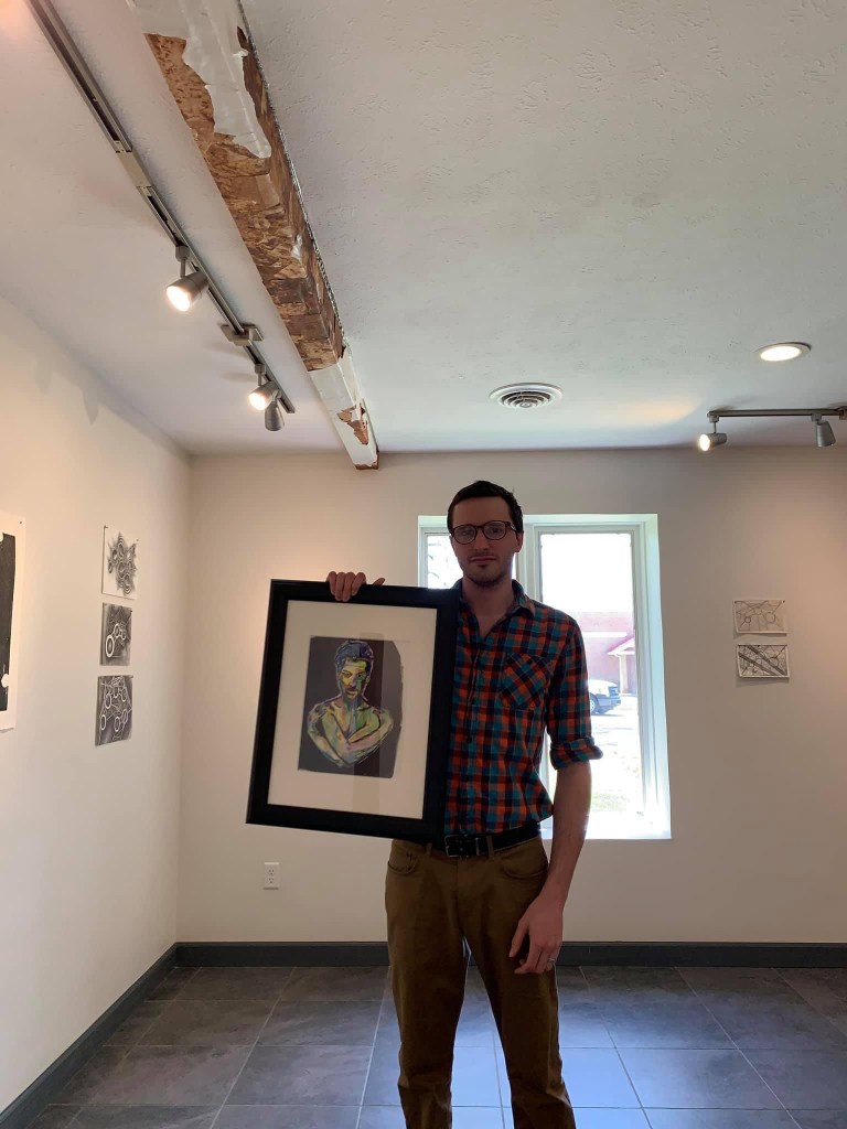 Artist Russell frantom holding one of his paintings in an art gallery
