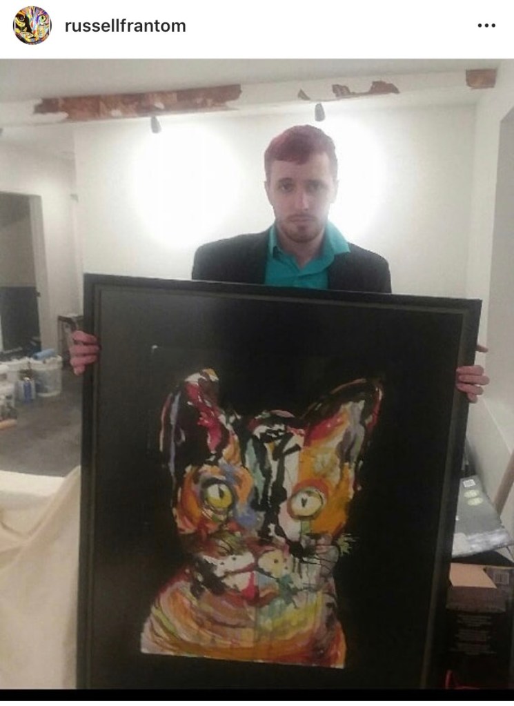 Visual Artist Russell Frantom holds one of his cat paintings in an art gallery. 2017